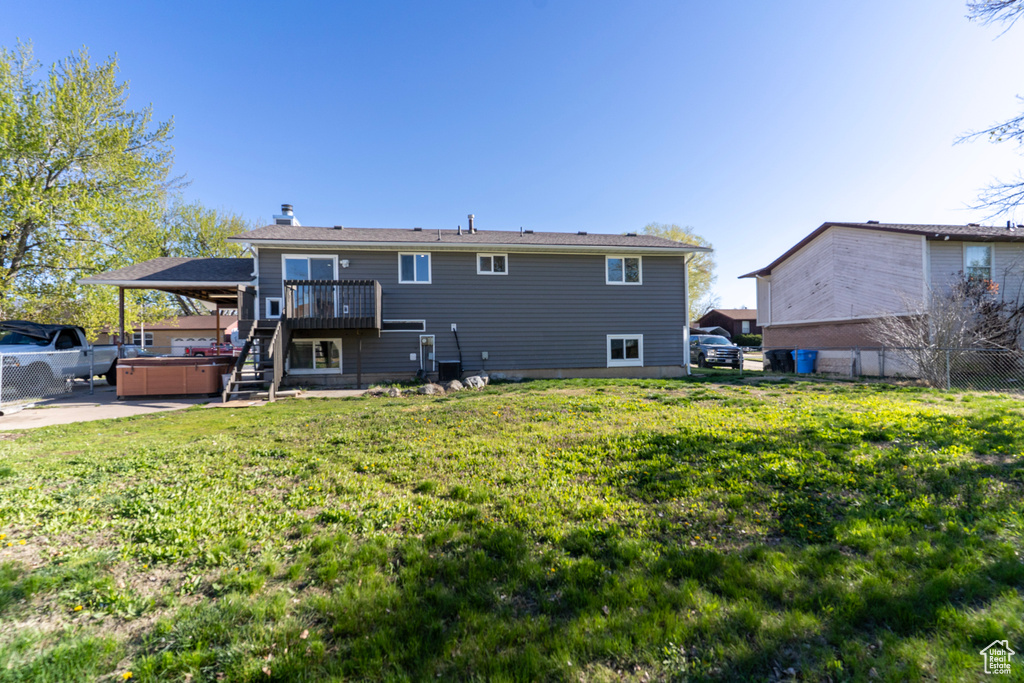 Rear view of house featuring a deck, stairway, fence, a hot tub, and a lawn