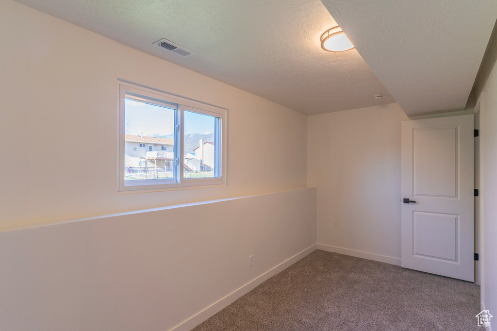 Carpeted empty room with baseboards, visible vents, and a textured ceiling