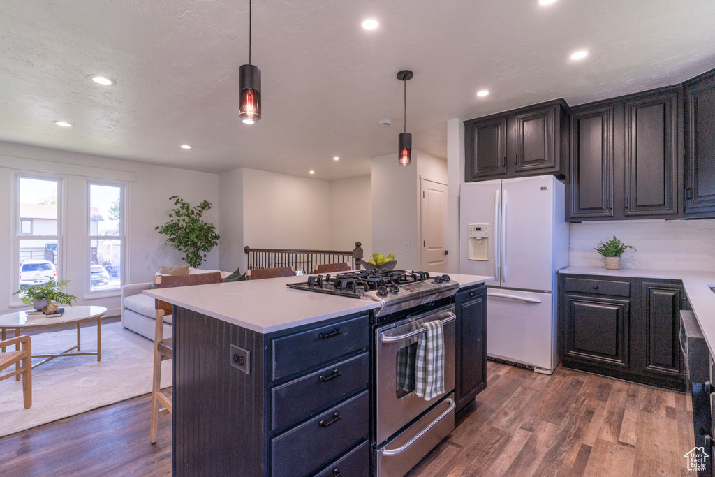 Kitchen with a kitchen bar, white fridge with ice dispenser, a kitchen island, stainless steel gas stove, and wood finished floors