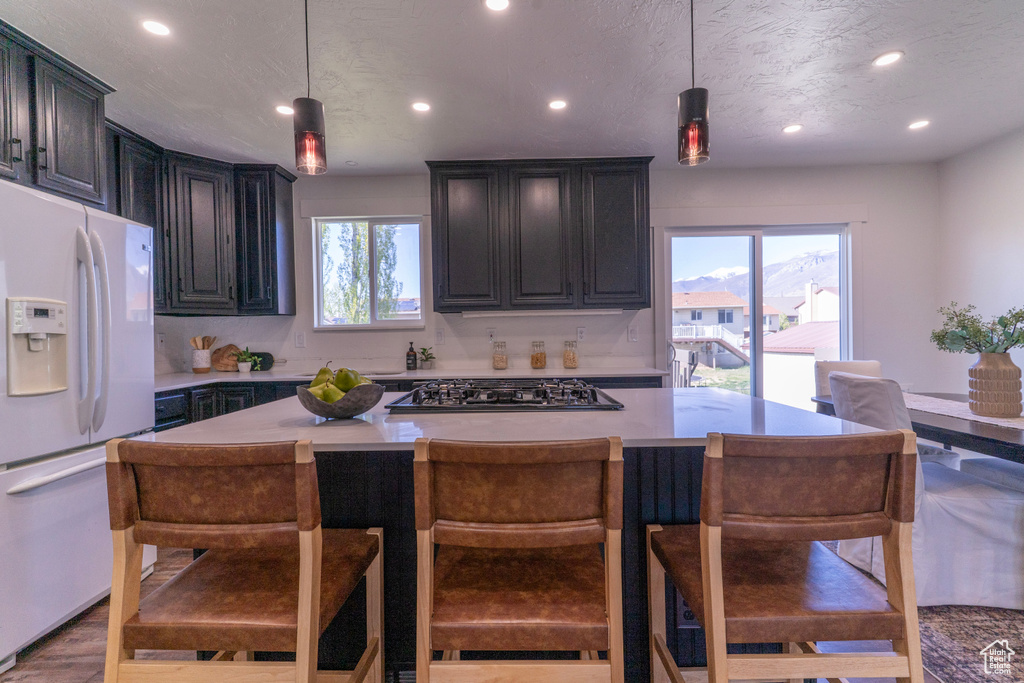 Kitchen with recessed lighting, white fridge with ice dispenser, stainless steel gas cooktop, and a wealth of natural light