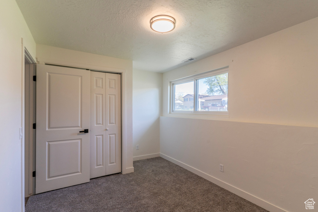 Unfurnished bedroom with a closet, visible vents, carpet, baseboards, and a textured ceiling