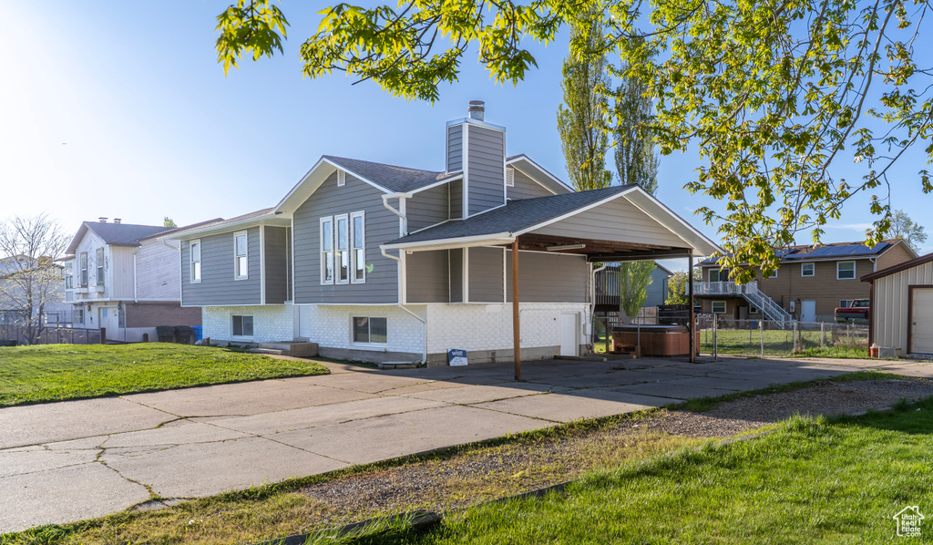 View of front of home featuring a chimney, a hot tub, an attached carport, a front lawn, and concrete driveway