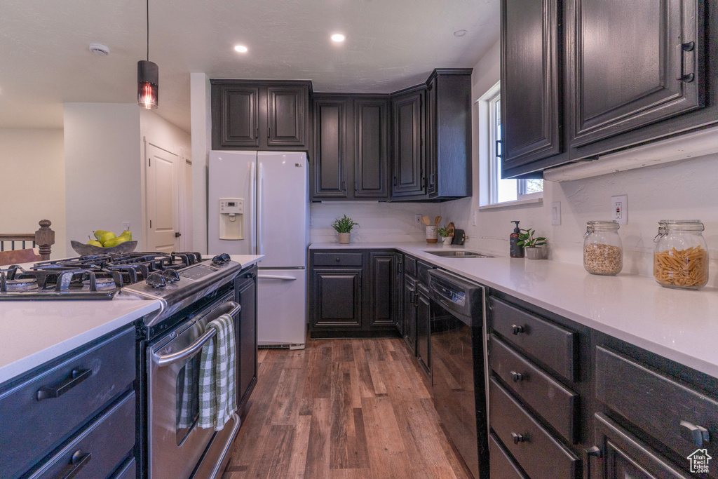 Kitchen with dark wood-style flooring, white fridge with ice dispenser, light countertops, dishwasher, and stainless steel gas range oven