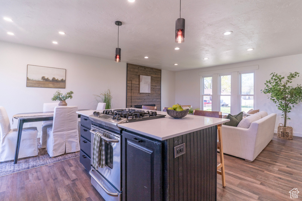 Kitchen with dark wood-style floors, stainless steel gas stove, open floor plan, a kitchen bar, and a fireplace