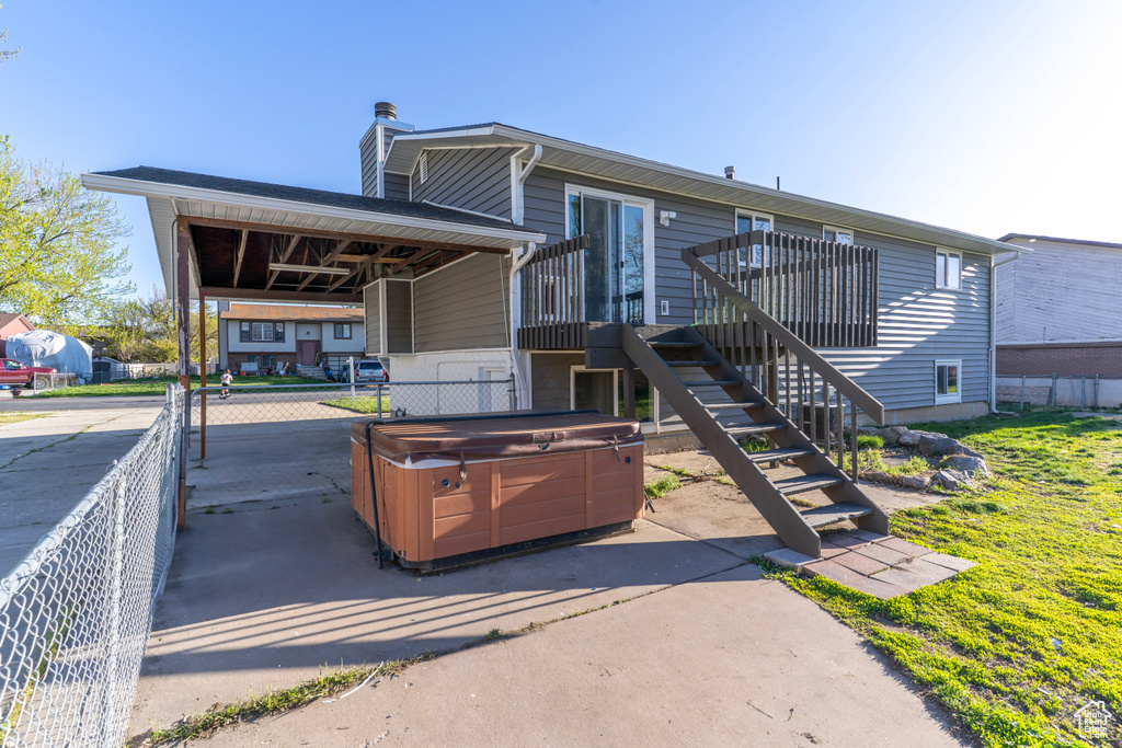 Rear view of house with a chimney, fence, a patio area, a carport, and a hot tub