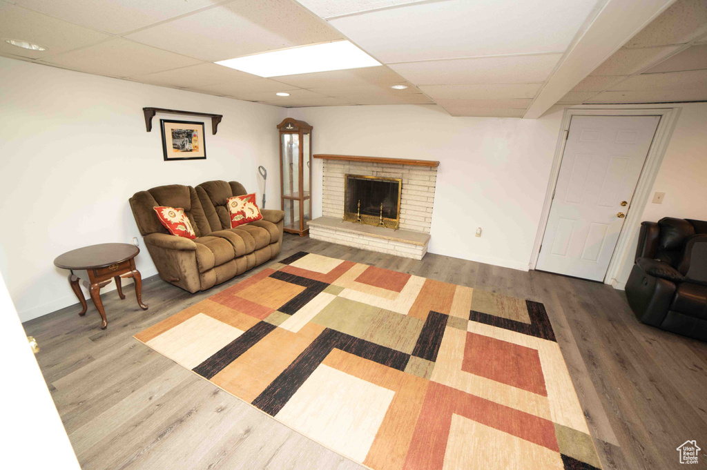 Living room featuring wood finished floors, baseboards, a drop ceiling, and a fireplace