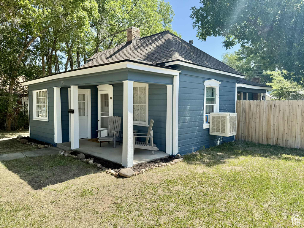 View of front facade with a chimney, a porch, roof with shingles, and cooling unit