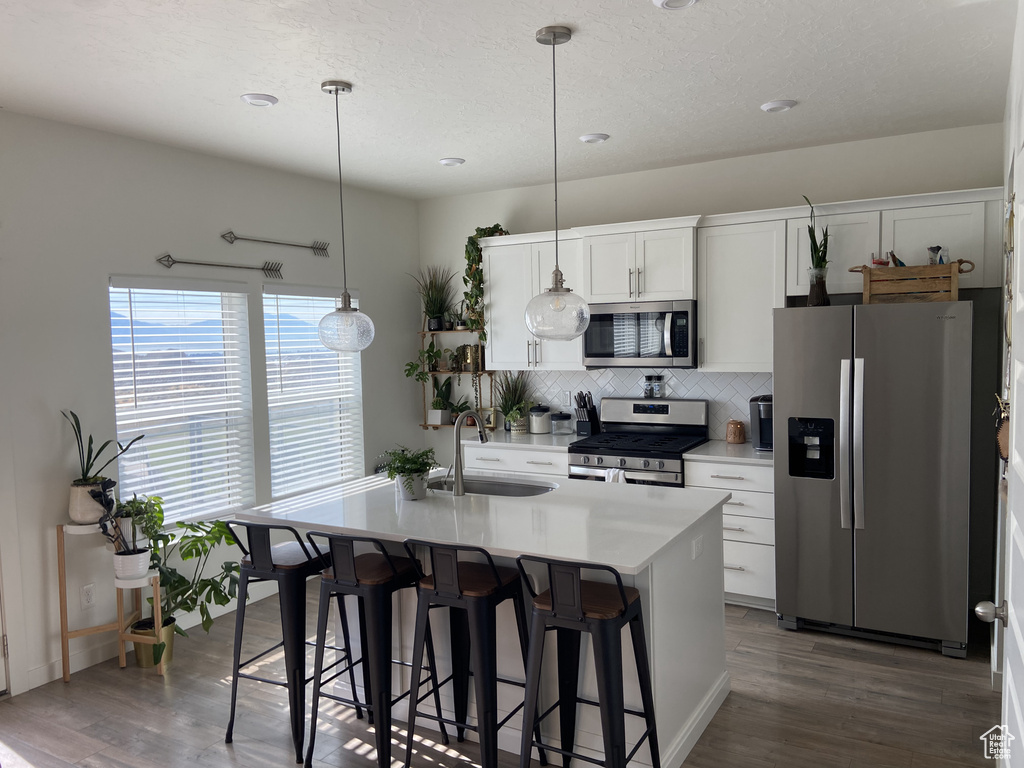 Kitchen featuring a kitchen breakfast bar, wood finished floors, a sink, tasteful backsplash, and appliances with stainless steel finishes