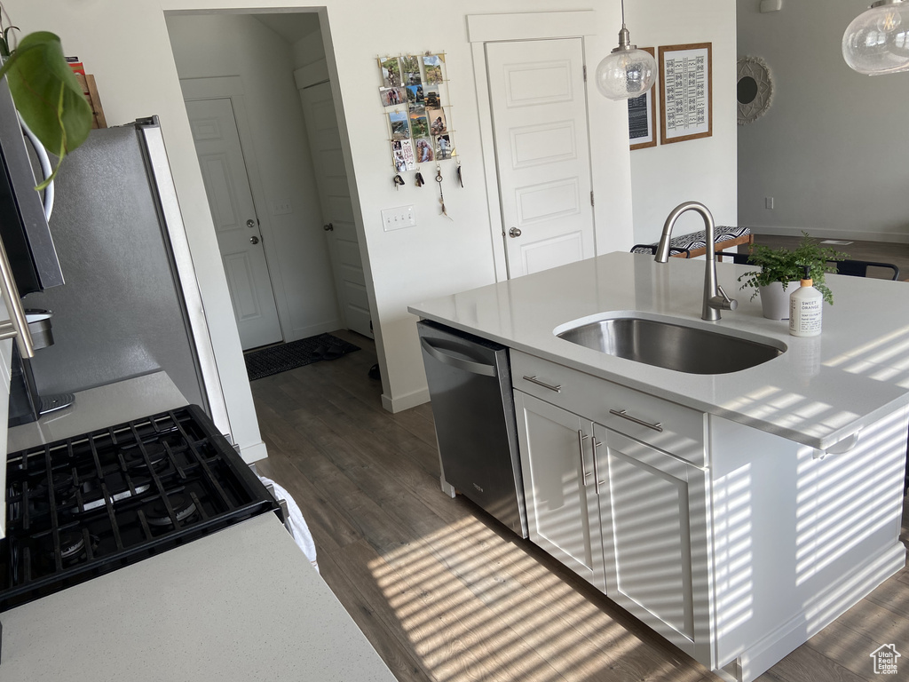 Kitchen with stainless steel dishwasher, a sink, light countertops, decorative light fixtures, and dark wood-type flooring