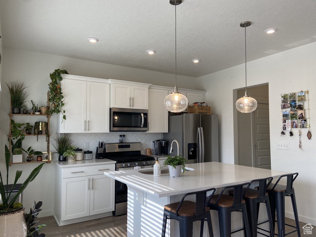 Kitchen featuring a kitchen island with sink, a kitchen bar, decorative backsplash, light countertops, and appliances with stainless steel finishes
