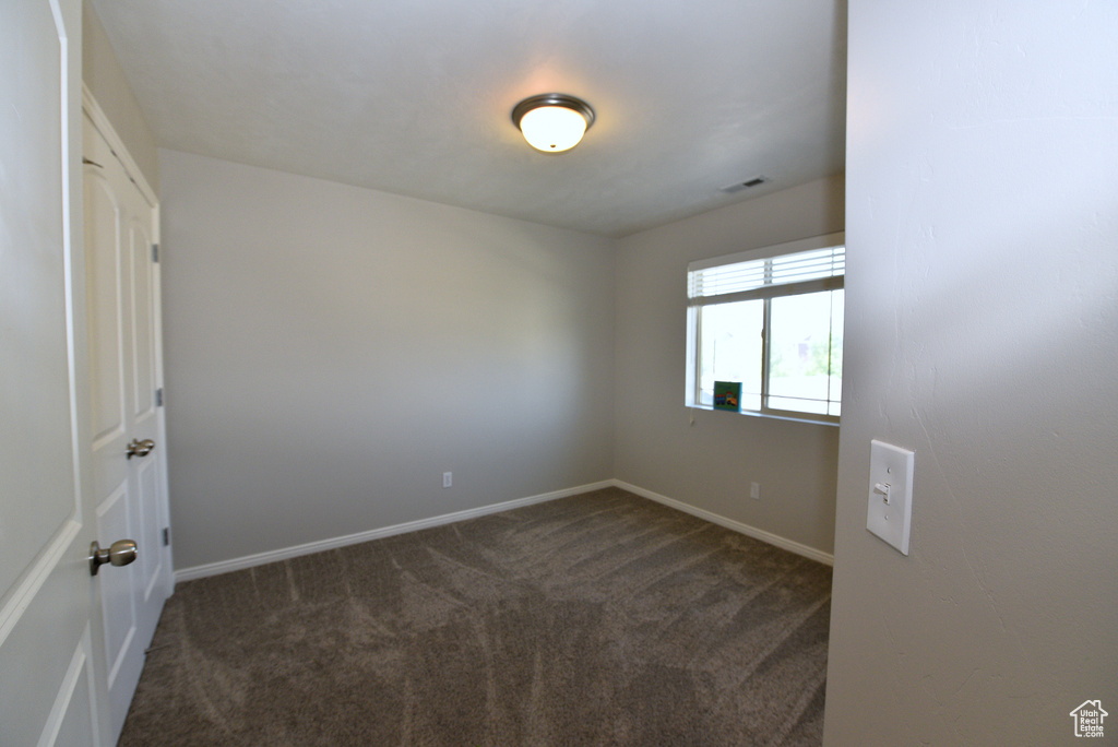 Unfurnished room featuring dark colored carpet and baseboards
