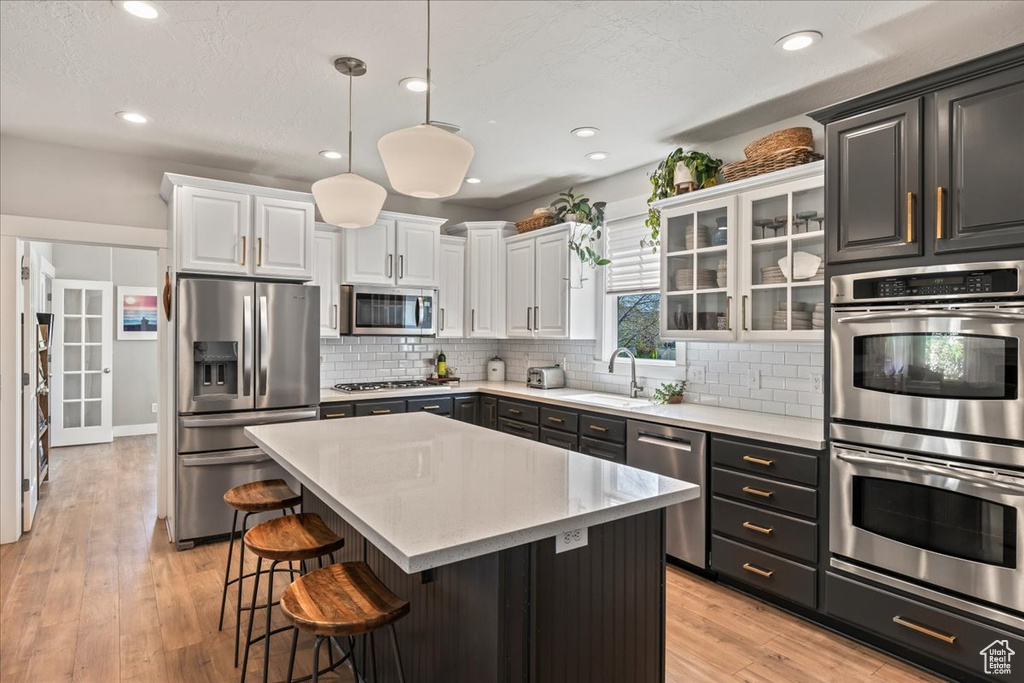 Kitchen with a sink, decorative backsplash, a breakfast bar area, white cabinets, and appliances with stainless steel finishes