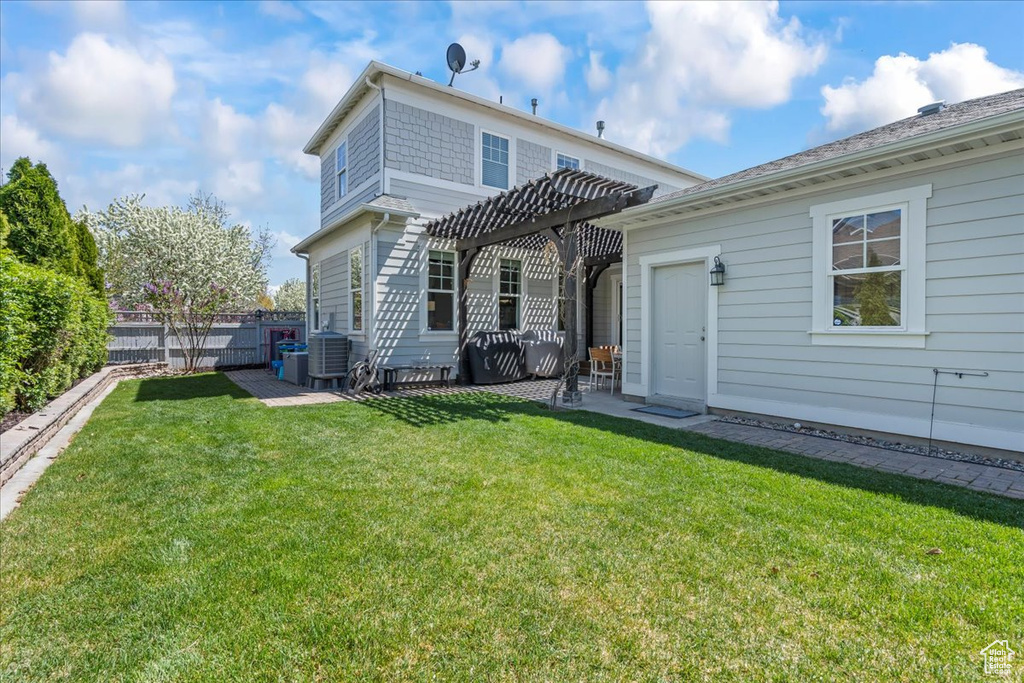 Rear view of house featuring central AC unit, a pergola, a lawn, fence, and a patio