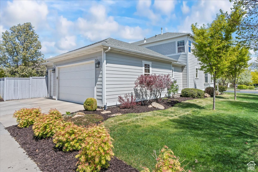View of property exterior with roof with shingles, a gate, concrete driveway, an attached garage, and a lawn