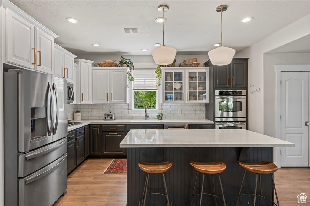 Kitchen featuring a sink, stainless steel appliances, light wood finished floors, light countertops, and a kitchen bar