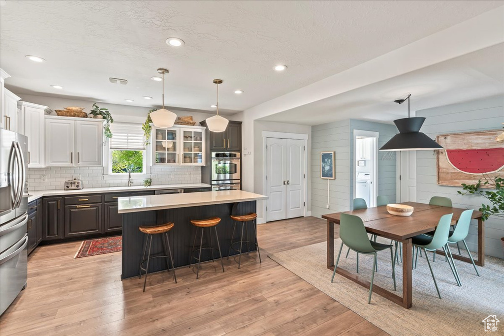 Kitchen featuring a kitchen breakfast bar, light wood-type flooring, light countertops, a kitchen island, and appliances with stainless steel finishes
