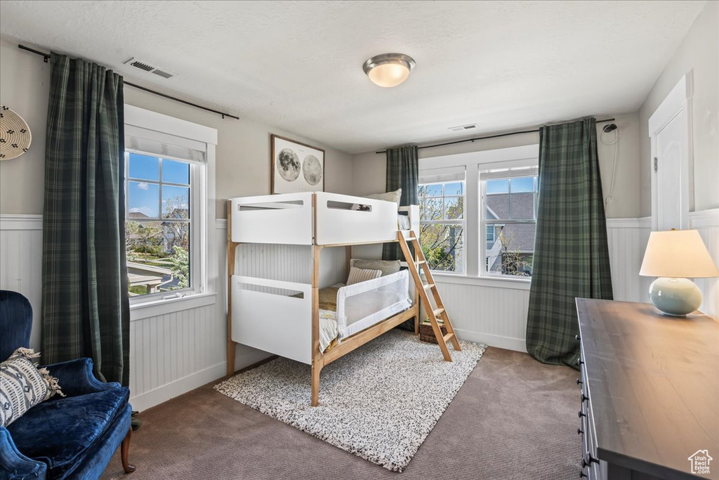 Carpeted bedroom featuring wainscoting and visible vents