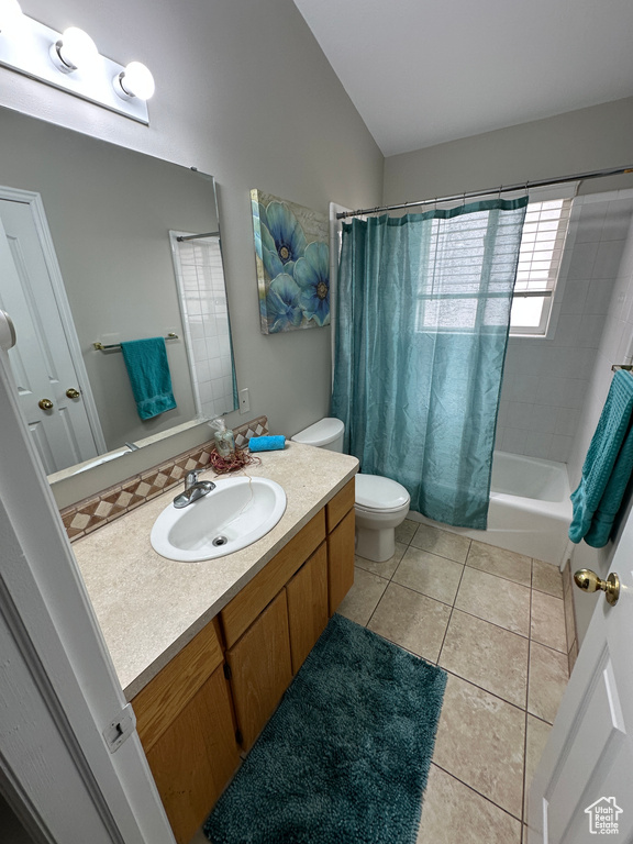 Bathroom with lofted ceiling, tile patterned floors, toilet, vanity, and shower / tub combo with curtain