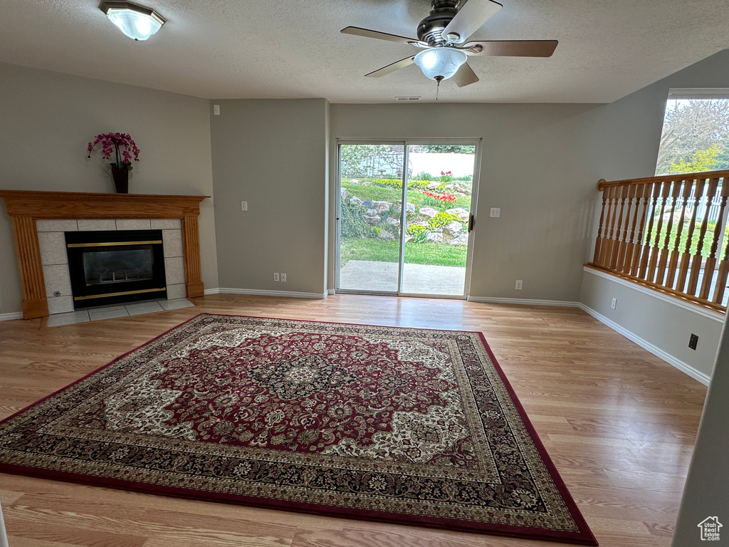 Unfurnished living room with a tile fireplace, wood finished floors, baseboards, a textured ceiling, and ceiling fan