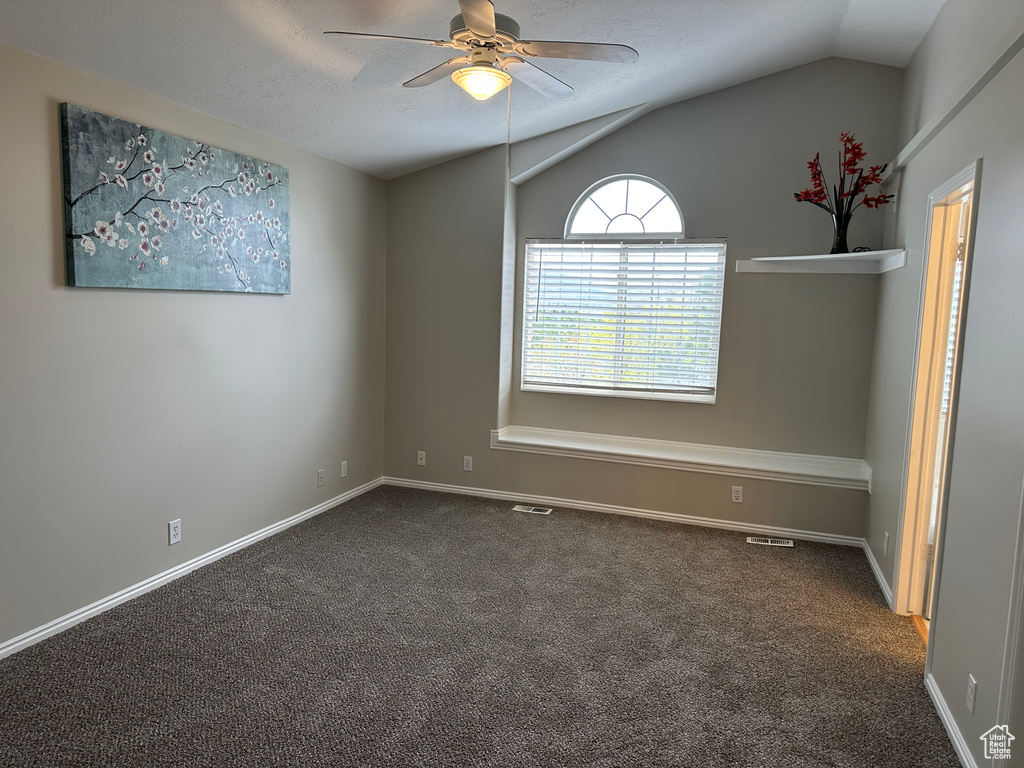Empty room featuring dark colored carpet, vaulted ceiling, visible vents, baseboards, and a ceiling fan