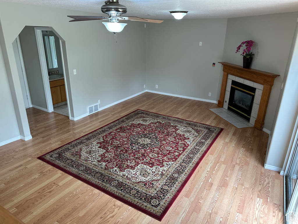 Living area with ceiling fan, a tile fireplace, visible vents, and light wood-style flooring