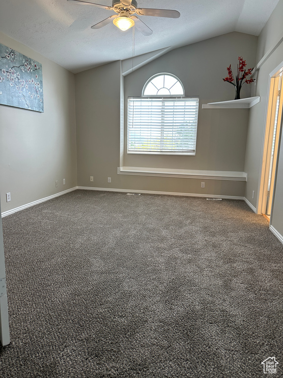 Carpeted empty room featuring attic access, lofted ceiling, a ceiling fan, and baseboards