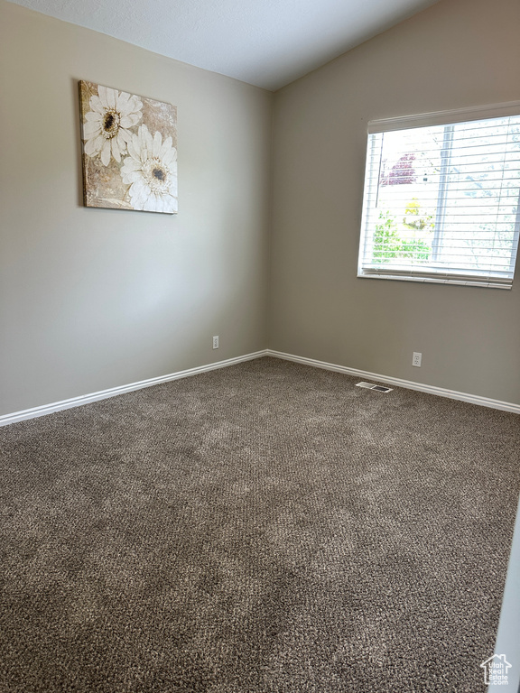 Empty room with vaulted ceiling, visible vents, carpet flooring, and baseboards
