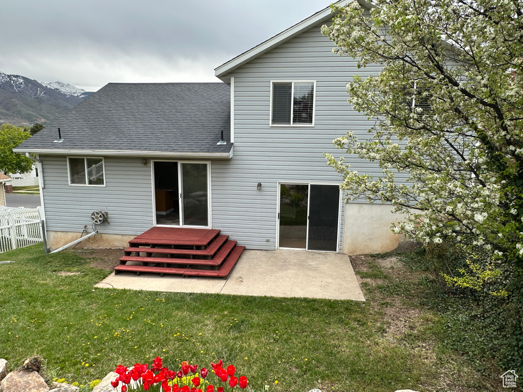 Rear view of house featuring roof with shingles, a mountain view, fence, a patio area, and a yard