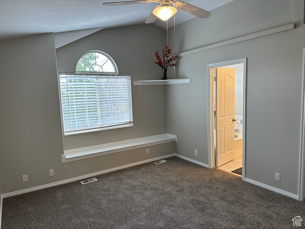 Carpeted empty room featuring baseboards, vaulted ceiling, visible vents, and ceiling fan