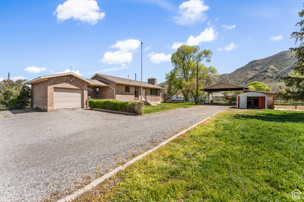 Single story home with an attached garage, gravel driveway, a front yard, and a chimney