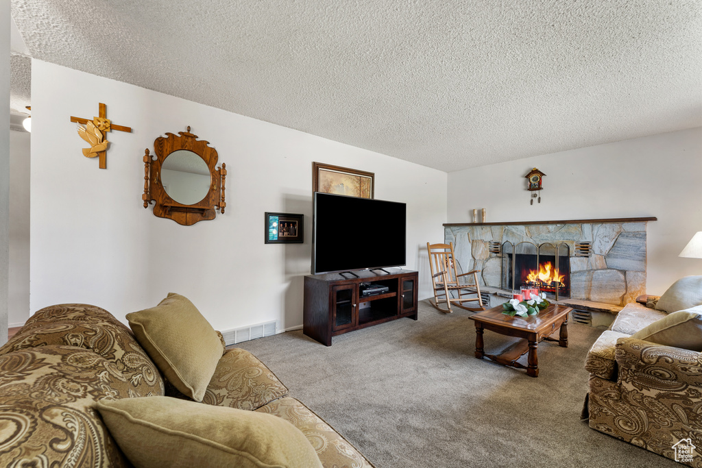 Carpeted living area featuring a fireplace, visible vents, and a textured ceiling