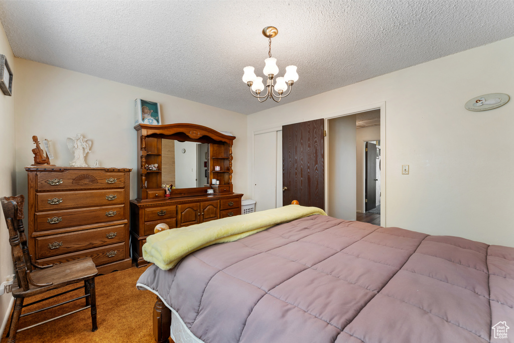 Bedroom with a textured ceiling, carpet, a notable chandelier, and a closet