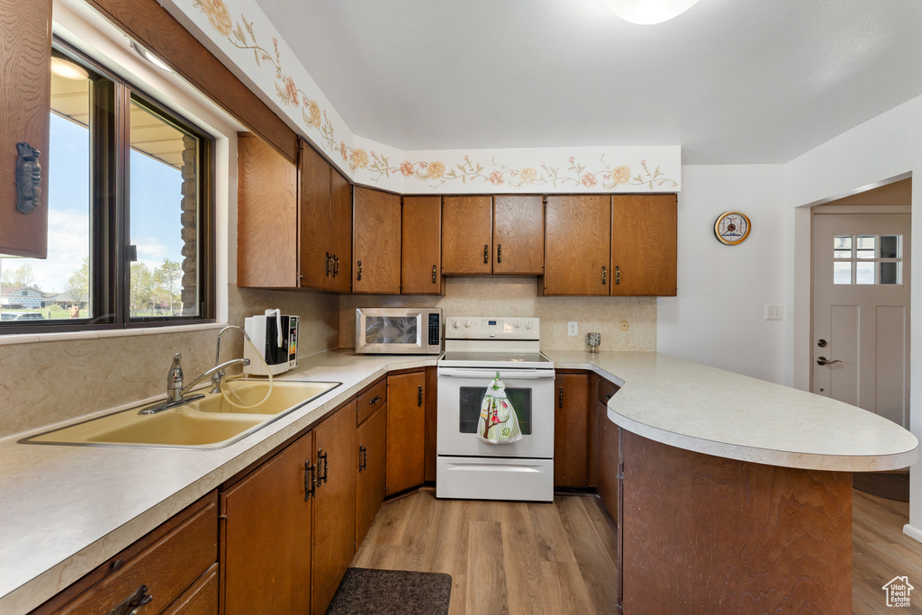 Kitchen featuring white range with electric stovetop, a sink, light countertops, stainless steel microwave, and a peninsula