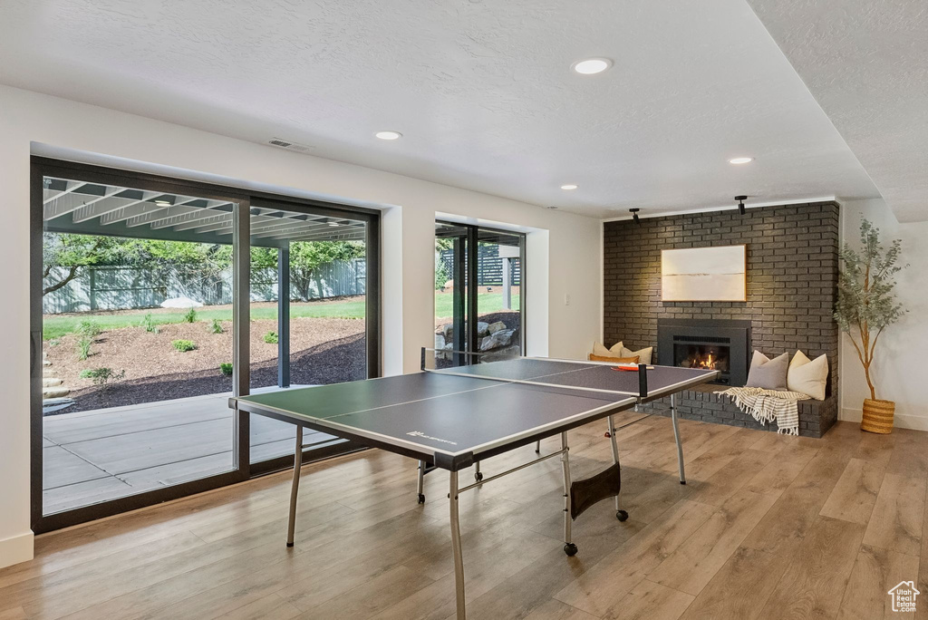 Rec room with recessed lighting, a brick fireplace, baseboards, light wood-style flooring, and a textured ceiling
