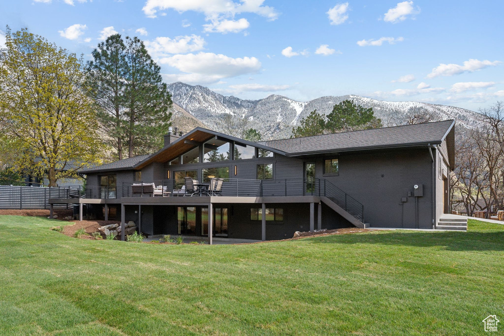 Rear view of property featuring a yard, a deck with mountain view, a chimney, and stairs