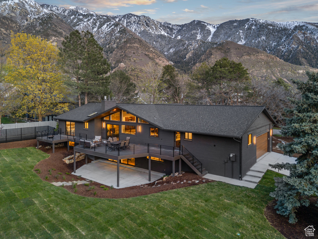 Rear view of property with fence, a deck with mountain view, a yard, and a shingled roof