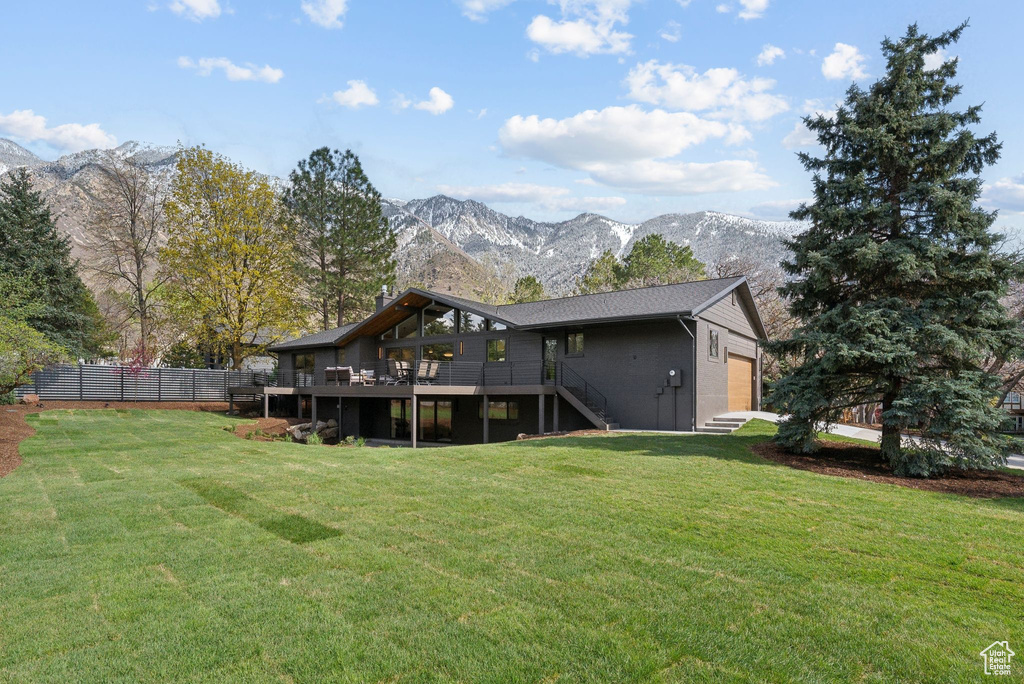 Rear view of property with stairs, a deck with mountain view, fence, a lawn, and a garage