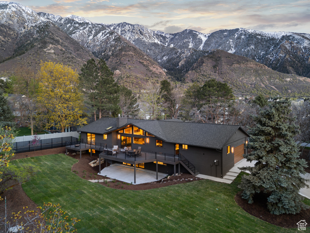 Rear view of property featuring a deck with mountain view, a lawn, and fence