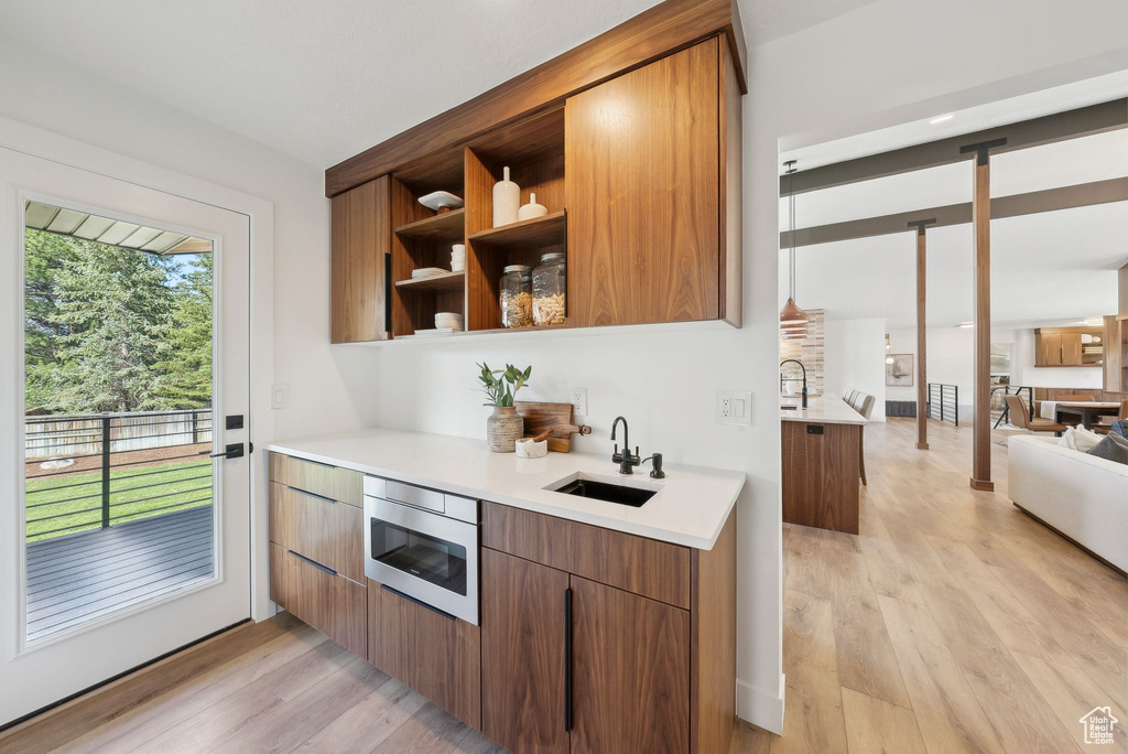 Kitchen with light wood-style flooring, oven, a sink, brown cabinets, and light countertops
