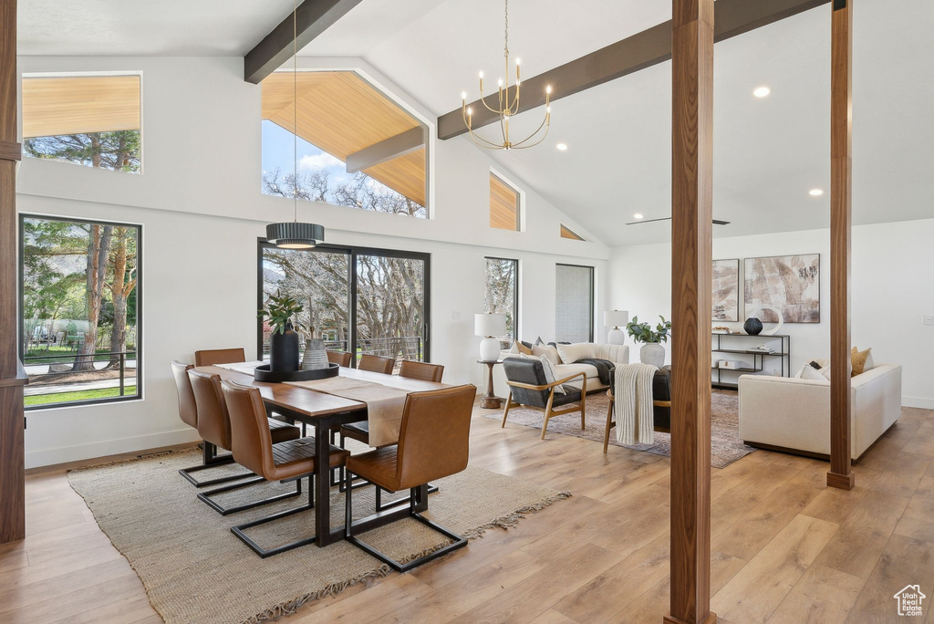 Dining room with light wood finished floors, beam ceiling, baseboards, an inviting chandelier, and high vaulted ceiling