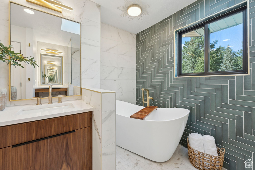 Bathroom featuring tile walls, a freestanding tub, vanity, and a healthy amount of sunlight