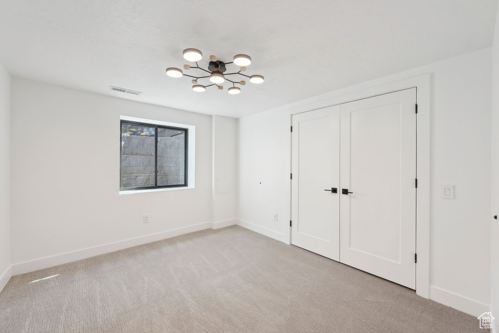 Unfurnished bedroom featuring baseboards, an inviting chandelier, visible vents, and light carpet