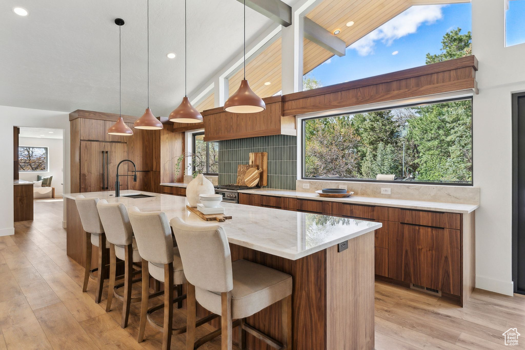 Kitchen featuring a kitchen island with sink, a sink, light wood-style floors, brown cabinets, and light stone countertops