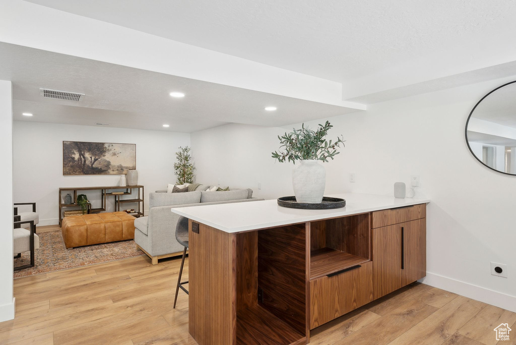 Kitchen with light wood finished floors, light countertops, visible vents, a peninsula, and a kitchen bar
