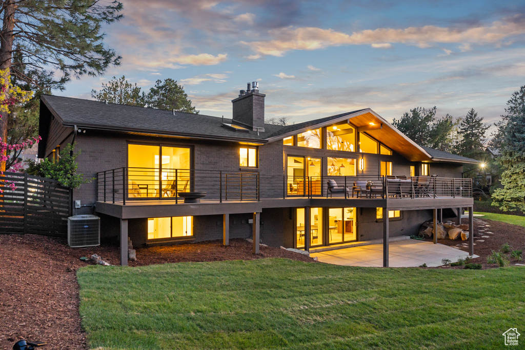 Back of house at dusk featuring a patio area, a chimney, brick siding, and a yard