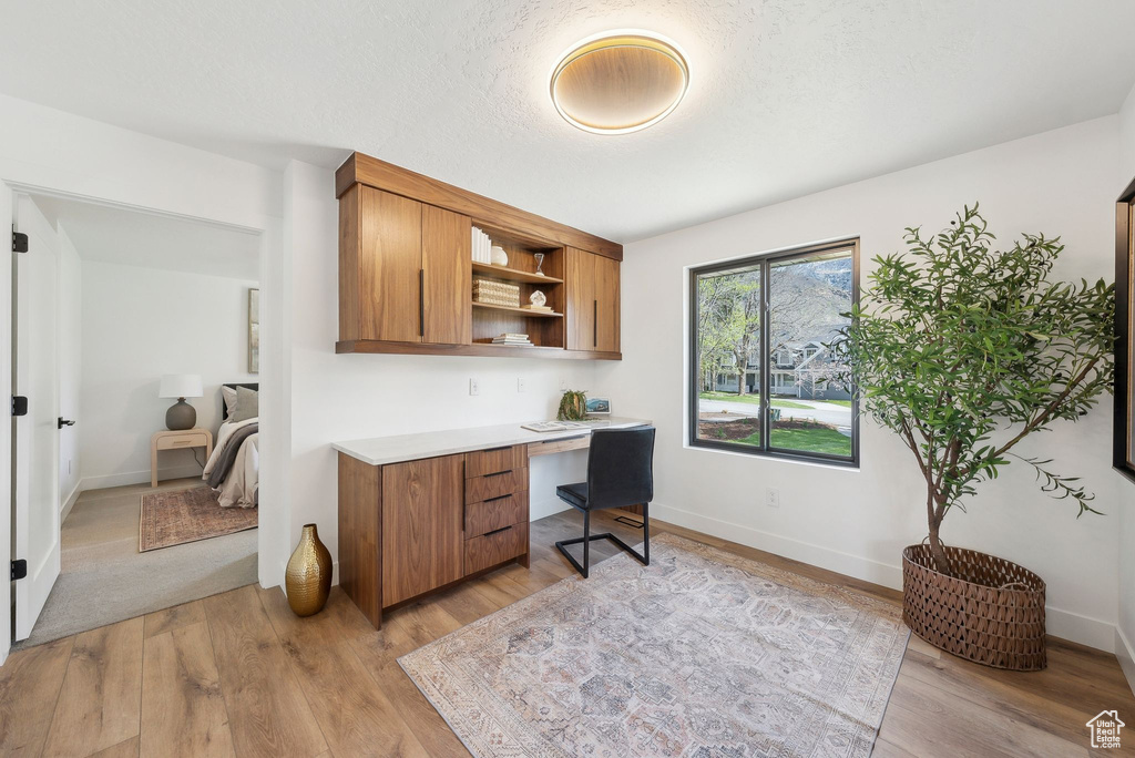 Office area with baseboards, light wood-style floors, and built in desk