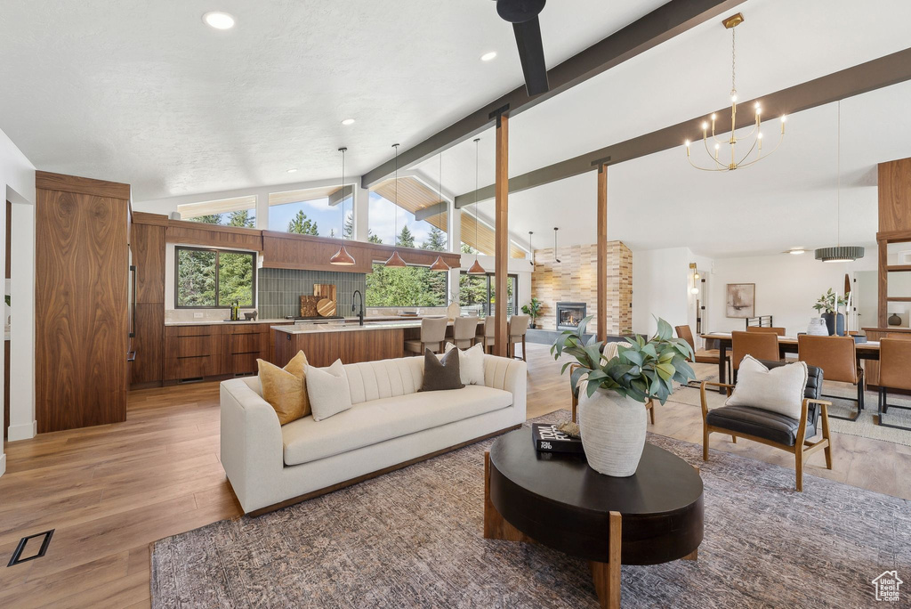 Living area featuring light wood finished floors, vaulted ceiling with beams, an inviting chandelier, and recessed lighting