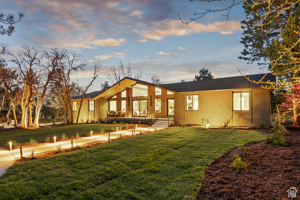 Back of property at dusk with a lawn