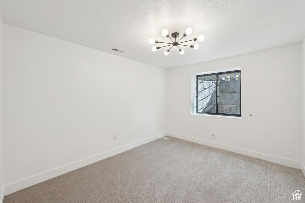 Spare room with baseboards, visible vents, an inviting chandelier, and light colored carpet