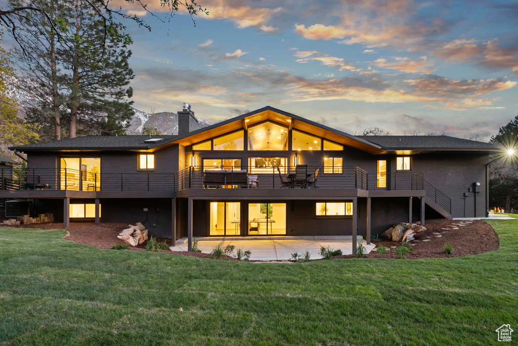 Rear view of property featuring a chimney, a wooden deck, a patio area, a lawn, and stairs